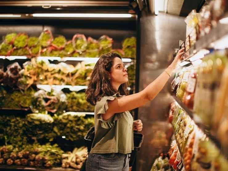 Donna che cerca alimenti nello scaffale di un supermercato
