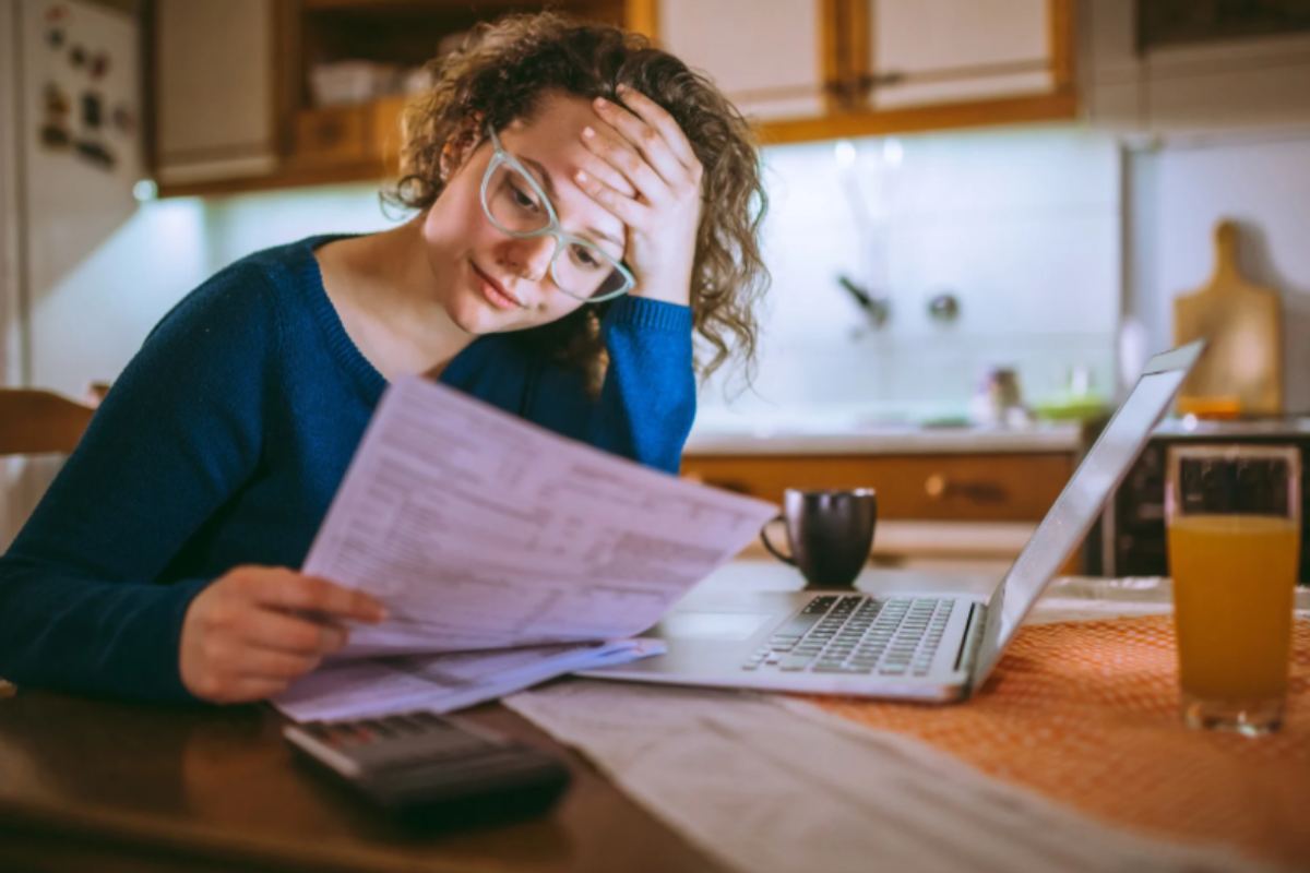 donna che legge una bolletta con aria preoccupata e una mano sulla fronte