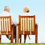 coppia di anziani seduta su sedie in legno di fronte al cielo