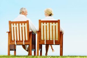 coppia di anziani seduta su sedie in legno di fronte al cielo