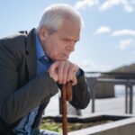 pensionato preoccupato con le mani su bastone