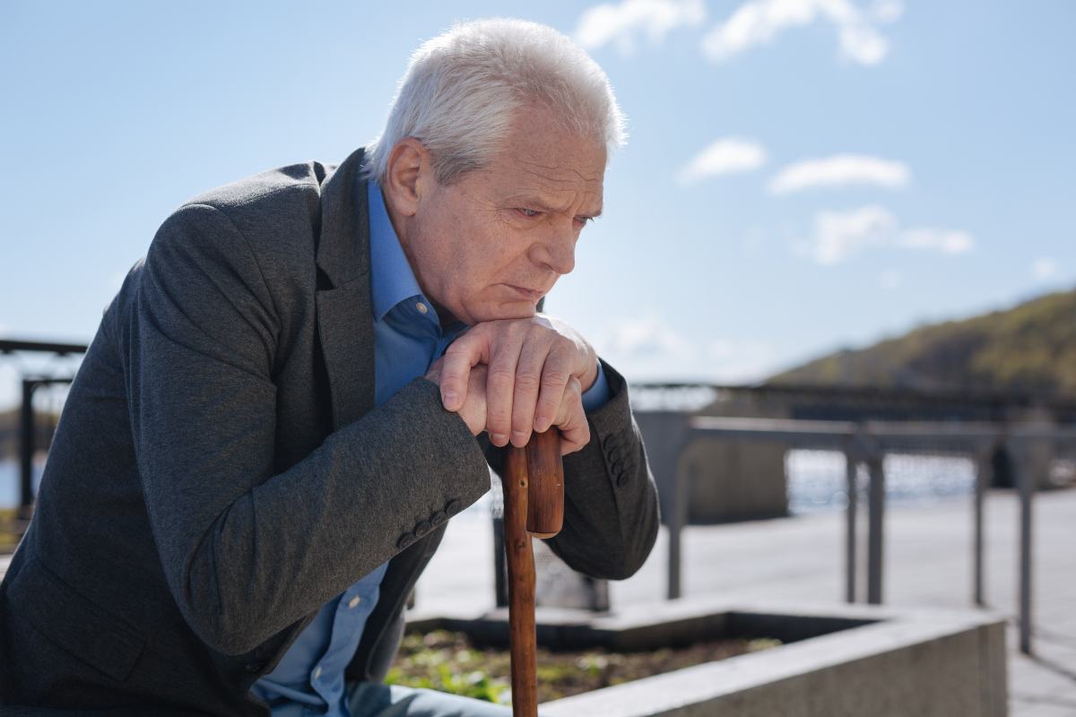 pensionato preoccupato con le mani su bastone