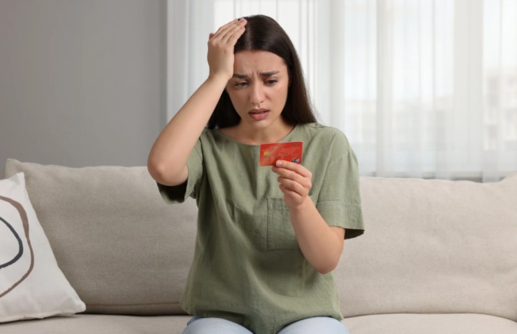 donna disperata con una mano sulla testa e nell'altra mano il bancomat
