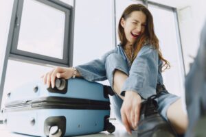 donna che sorride e strizza l'occhiolino seduta per terra accanto ad un trolley