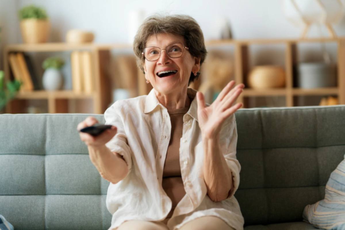 donna seduta sul divano sorridente con il telecomando in mano