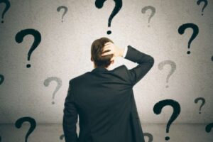 uomo di spalle con una mano dietro alla nuca circondato da punti interrogativi