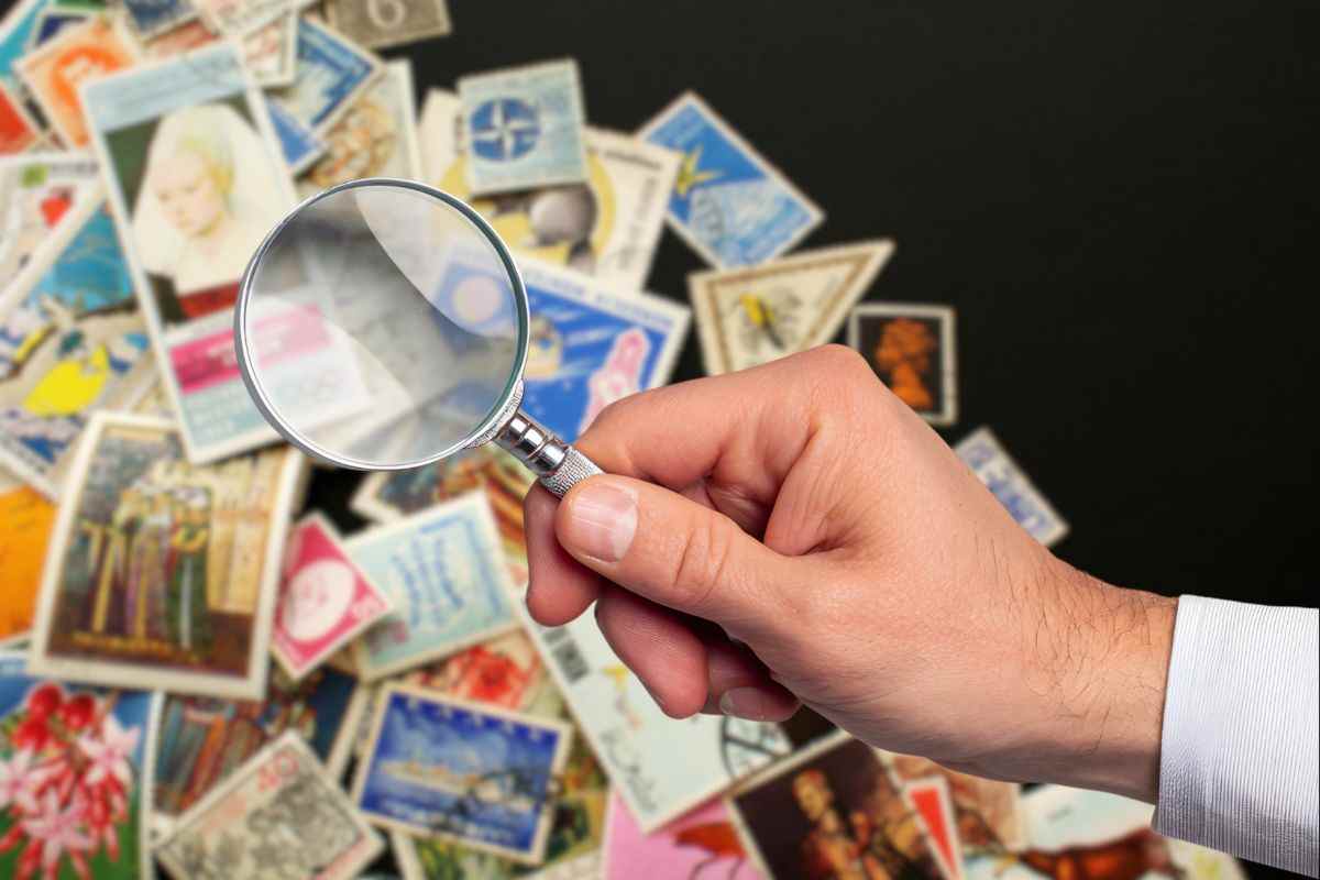 diversi francobolli su sfondo nero e mano di uomo che tiene lente d'ingrandimento