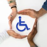 delle mani che formano un cerchio con in mezzo una persona disabile stilizzata