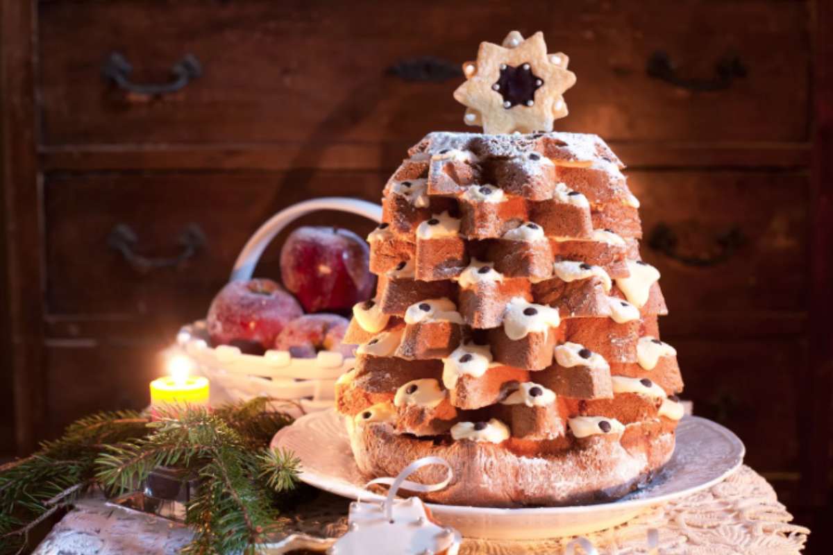 pandoro con sopra un biscotto a forma di stella e dietro delle mele rosse
