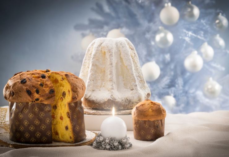 due panettoni e un pandoro davanti ad un albero di natale
