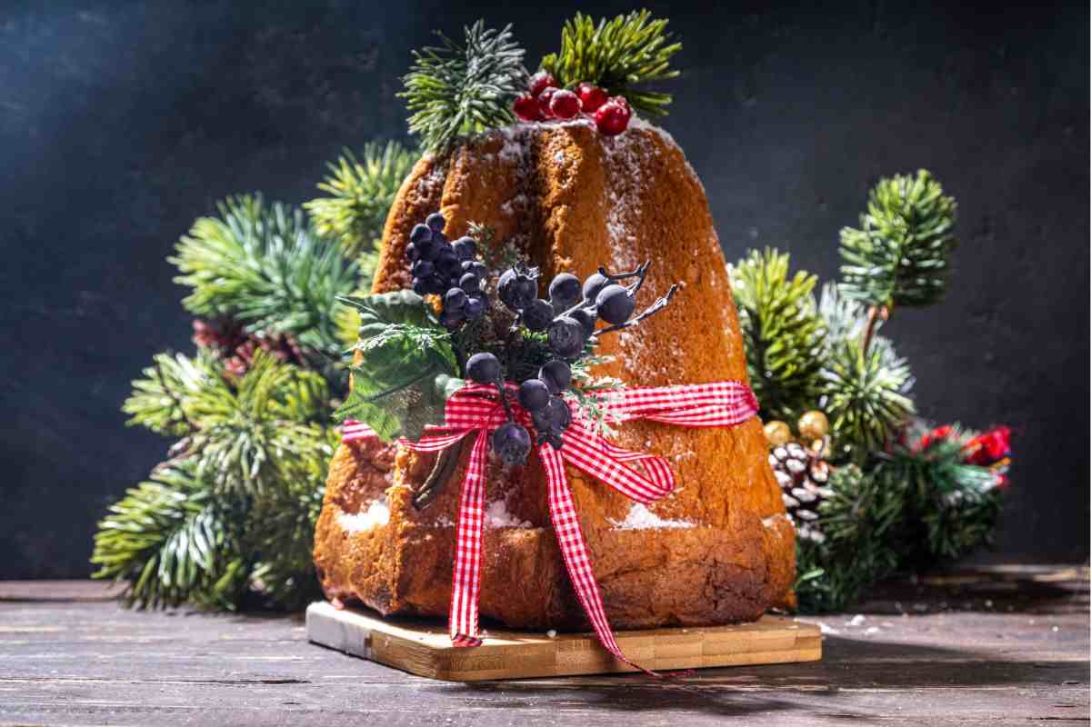pandoro poggiato su un tagliere in legno e decorato con rametti di abete e pigne