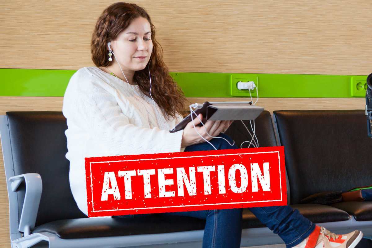 ragazza seduta che guarda il tablet collegato a una presa, scritta "attention"