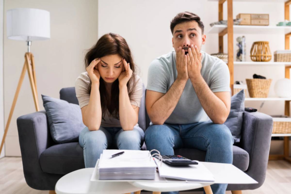 uomo e donna preoccupati seduti sul divano con davanti dei fogli e una calcolatrice